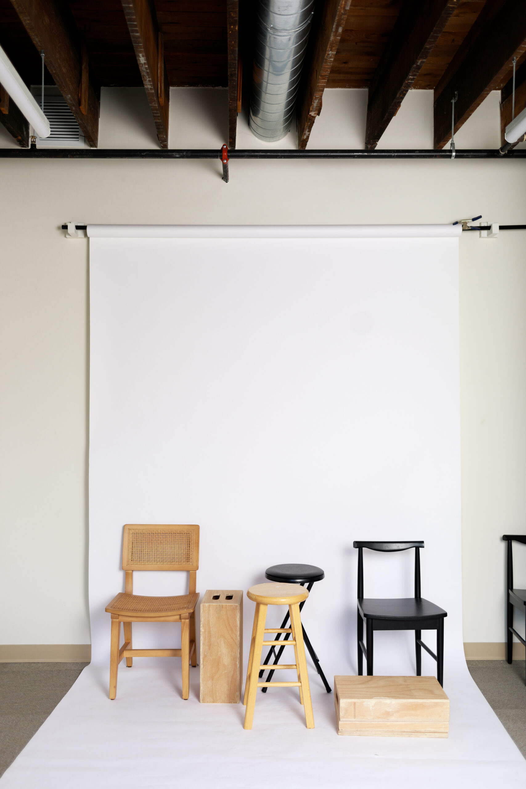 white backdrop in a photographers studio with multiple types of chairs set up for props