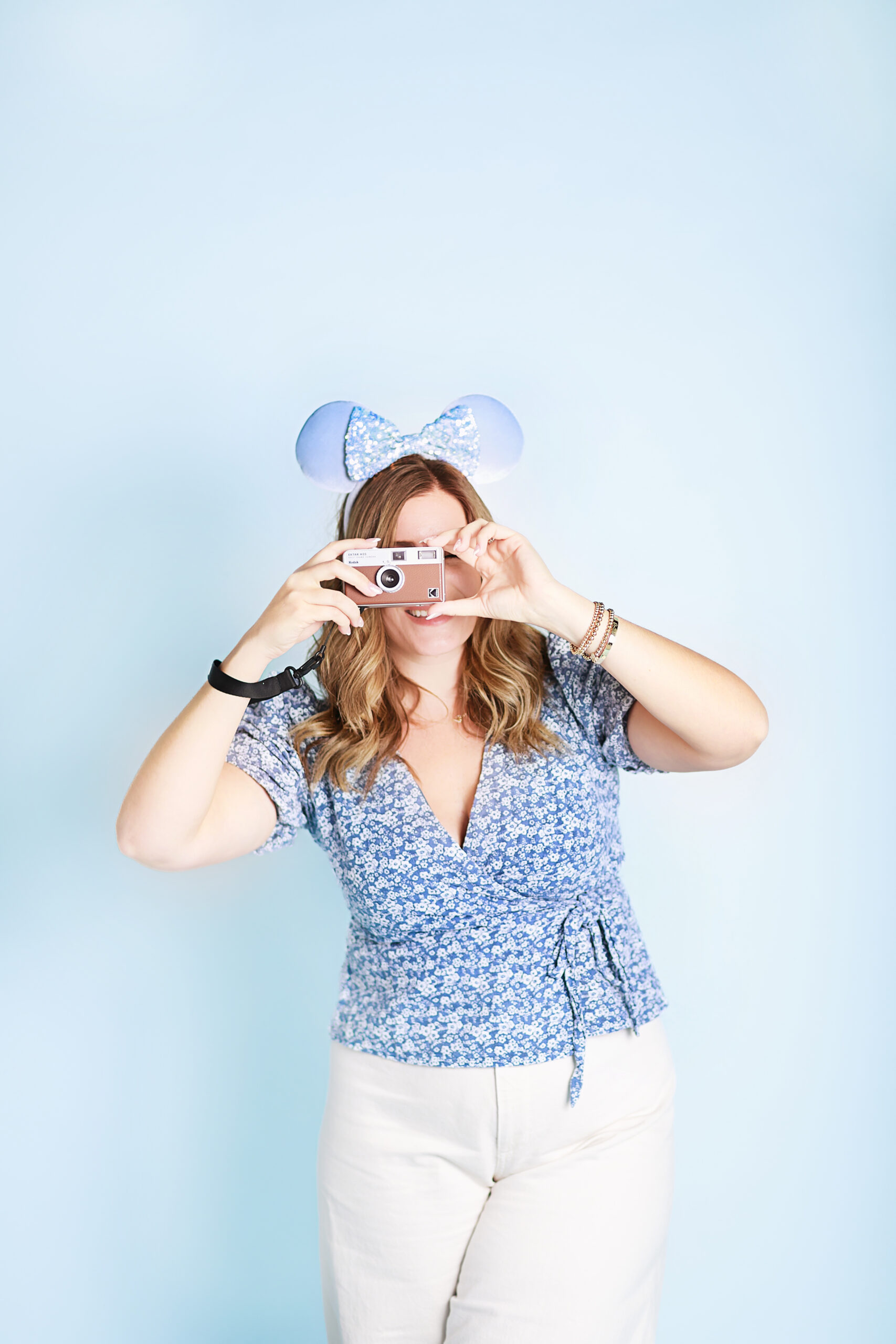 Disney travel planner smiling with a film camera and Mickey Mouse ears